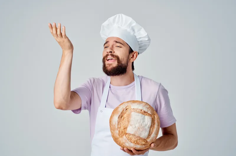 Бородатый мужчина в белом фартуке готовит еду