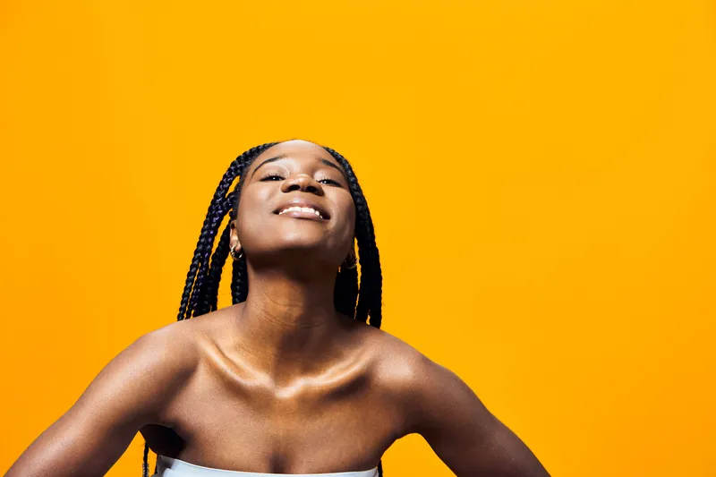 A joyful young African woman with braided hair smiles against a bright yellow background, radiating happiness and positivity