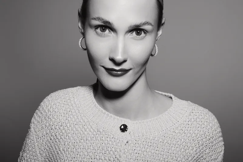 Close-up portrait of a fair-skinned Caucasian woman with earrings wearing a knitted sweater. Studio lighting highlights her confident expression and natural beauty in black and white.