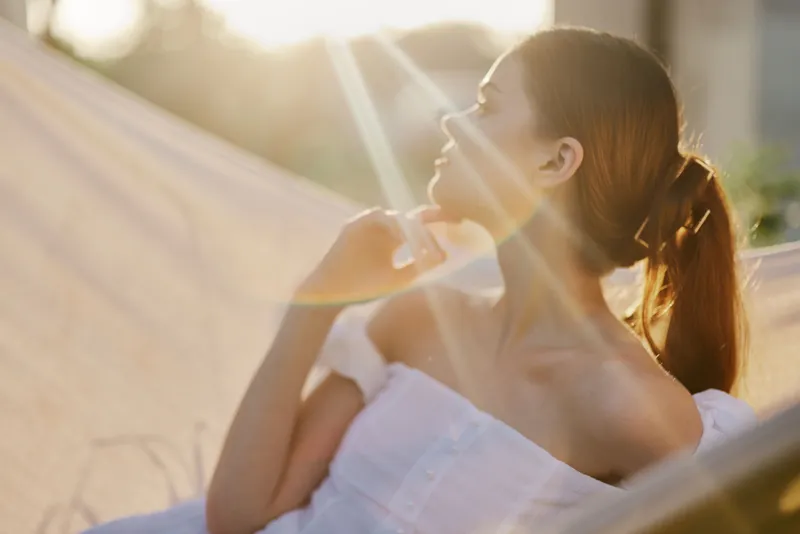 Elegant young woman in a sunlit hammock enjoying a peaceful moment, radiating relaxation and serenity in a warm summer setting