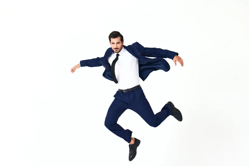 Улыбающийся мужчина в деловом костюме бежит и прыгает, взлетая вверх с открытым ртом, выражая счастье и удивление