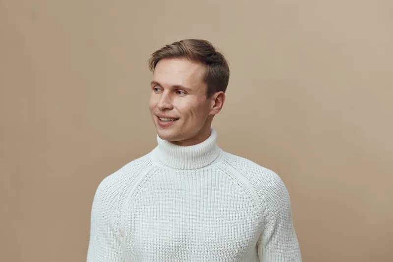 Smiling caucasian man wear white knitted turtleneck sweater look aside studio portrait beige background digital nomad concept