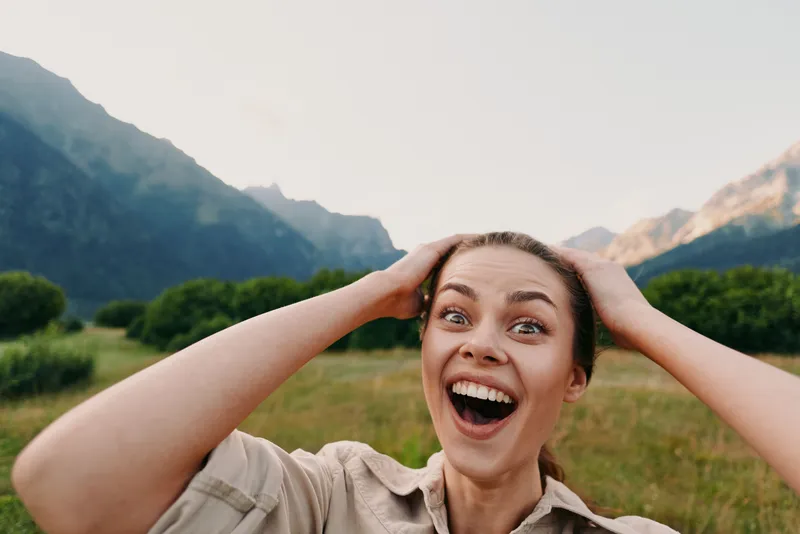 Cheerful woman outdoors, wide smile, hands on head, sunlight moment in a mountains valley, relaxed posture, vibrant natural colors, fresh air, happiness, lifestyle, nature, bright