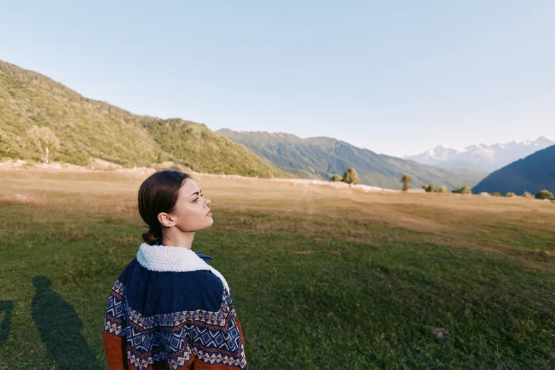 Woman portrait in mountains meadow landscape outdoors wearing patterned sweater, travel mood and thoughtful profile overlooking valley and horizon in scenic peaceful nature.