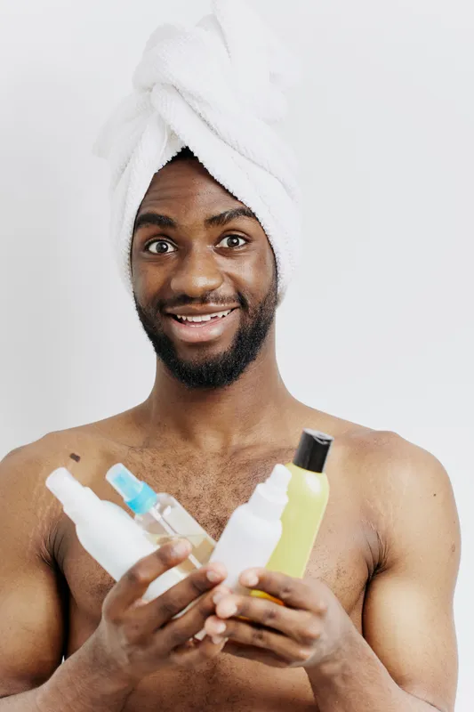 Мужчина в полотенце держит в руках флаконы с лосьоном и шампунем, готовясь к ежедневному уходу за собой с сосредоточенным выражением лица