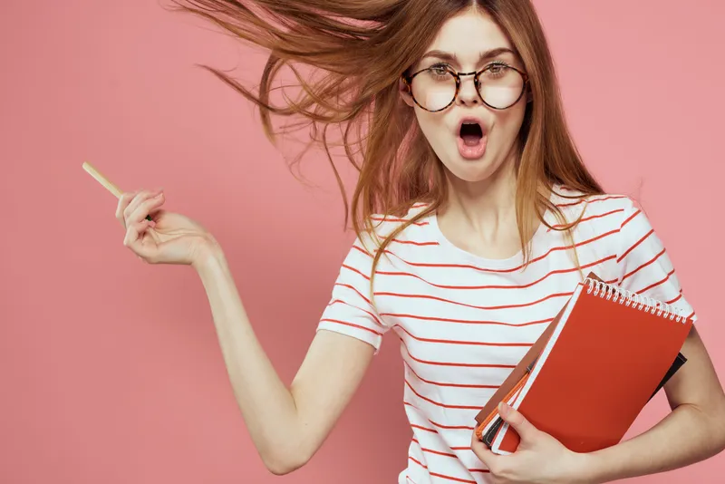 Молодая студентка с книгами на розовом фоне, в очках