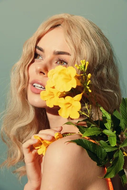 Красивая молодая женщина с blond-волосами, демонстрирующая яркие желтые цветы на нежном зеленом фоне, излучающая радость и безмятежность, идеально подходит для весенних проектов