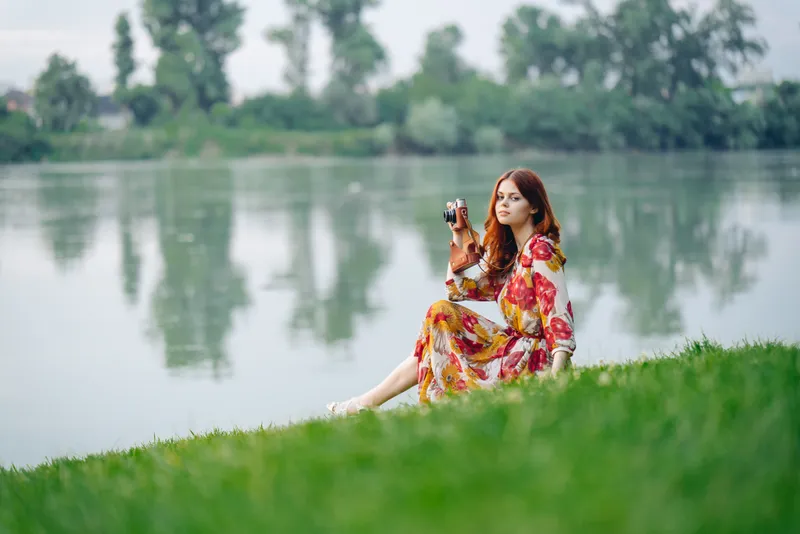 Женщина в платье с фотоаппаратом на природе занимается своим хобби — фотографией