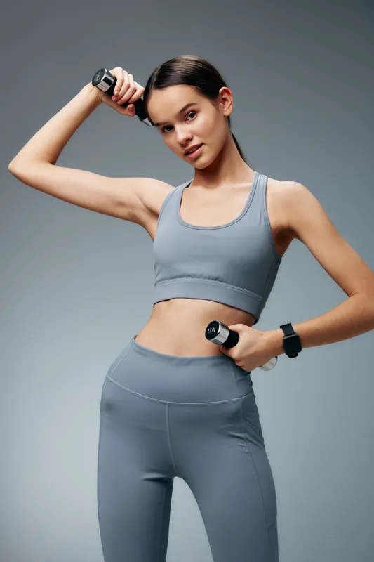 Female fitness enthusiast posing with dumbbells in gray athletic wear, showcasing strength, balance and focus during a dynamic workout for sport and health.