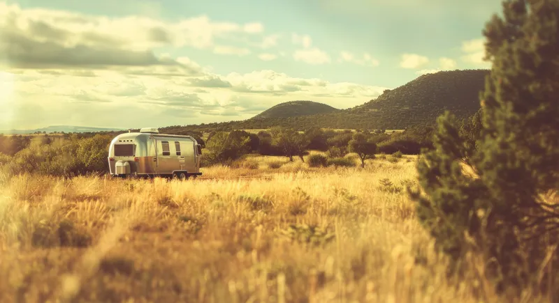 Живописный трейлер Airstream, припаркованный на травянистом поле на фоне величественных гор