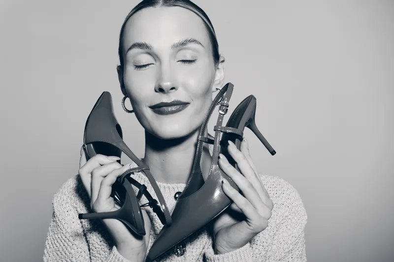 White woman with light skin holds a pair of high heel shoes near her face, eyes closed and smiling. Concept for fashion, style, footwear and happiness.