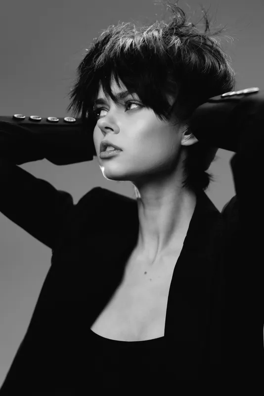 Black and white portrait of a thoughtful woman with short hair wearing a black jacket in studio lighting.