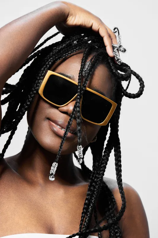 Stylish young woman with braided hair and sunglasses, embodying confidence and elegance, set against a minimalist background