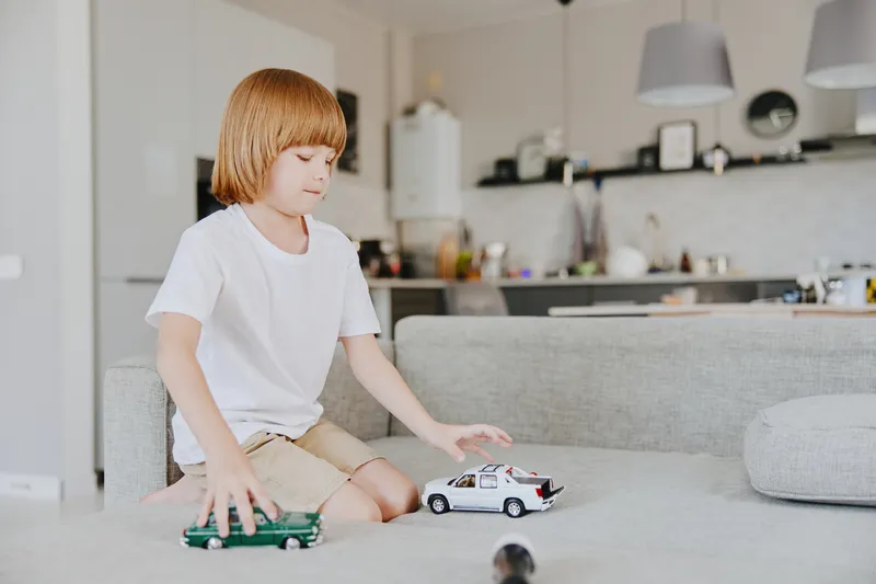 Young boy playing with toy cars in a modern living room, showcasing creativity and imagination in a playful atmosphere. Bright colors enhance the joyful mood.