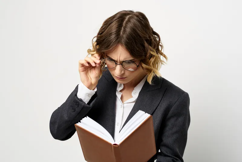 Женщина на работе с книгой в руке, светлый фон, классический костюм, очки, голова