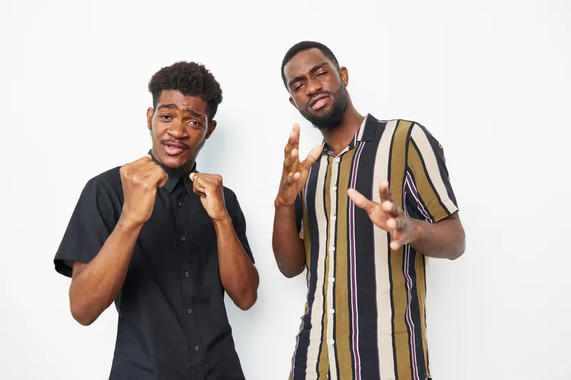 Two confident African American men posing together, expressing joy and camaraderie. Their vibrant outfits and playful gestures create a lively atmosphere full of energy.