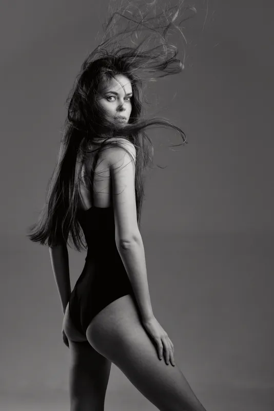 Black and white portrait of a woman with long hair wearing a black bodysuit looking back confidently.
