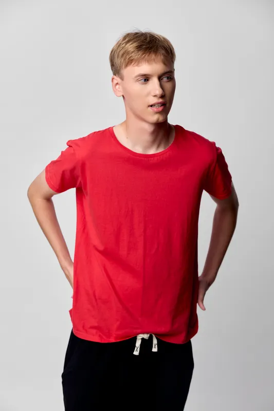 Young man in a red T-shirt stands with hands on hips, casual street style in a clean studio, relaxed mood, simple wardrobe, minimal background, everyday wear and confident presence
