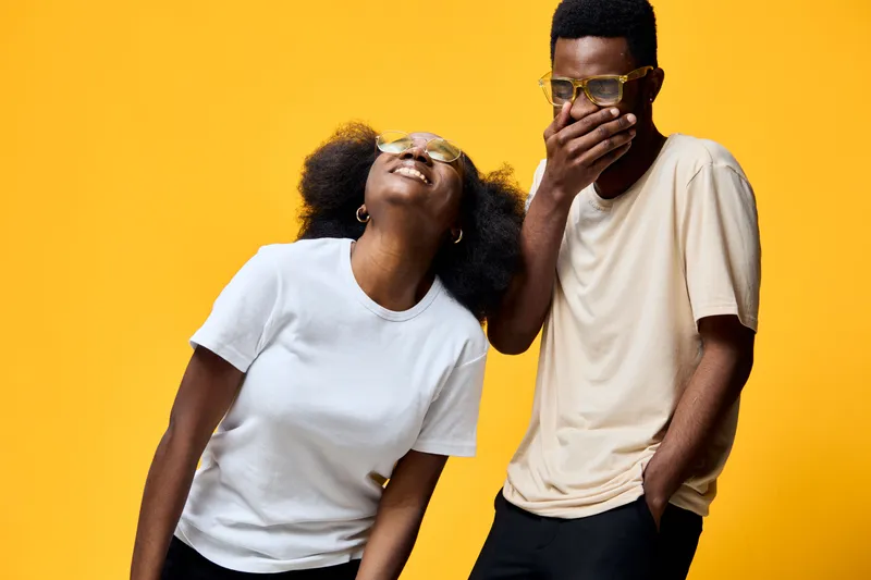 Two young adults joyfully sharing a moment against a vibrant yellow background, showcasing emotions of happiness and friendship, perfect for lifestyle and diversity themes