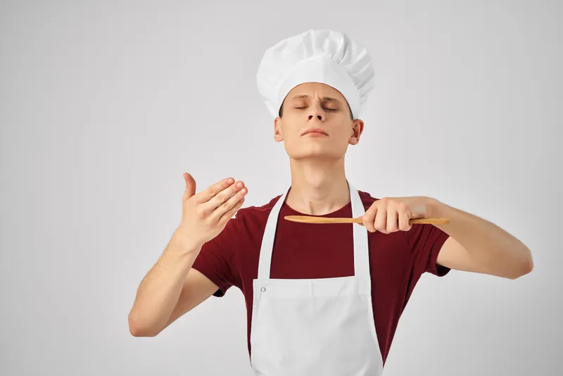 Мужчина в белом фартуке работает с кухонной утварью, занимаясь приготовлением пищи