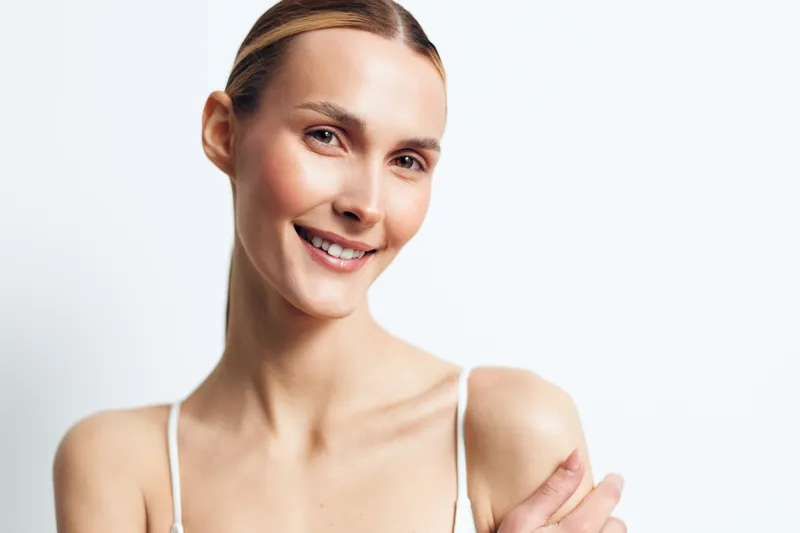 Woman portrait, smile, beauty, skincare, healthy young skin, clean bright background, confident friendly expression, soft studio light, close up, wellness mood, minimal composition