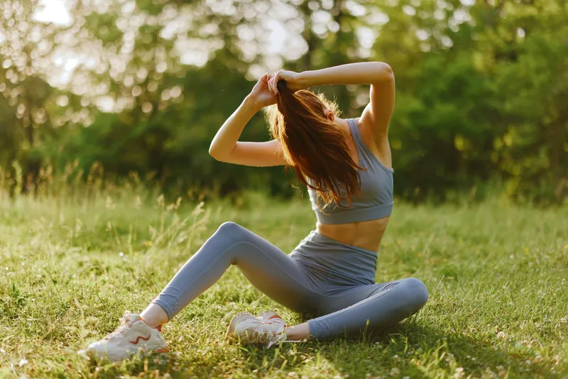 Athletic woman in a blue workout outfit stretching in a sunny green park, exuding confidence and determination while promoting a healthy lifestyle