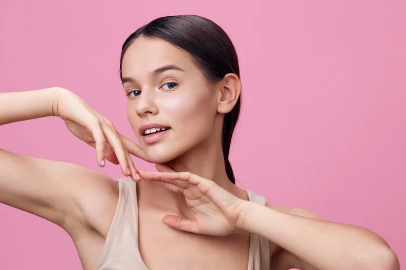 Young female model with a joyful expression on a pink background, showcasing beauty and confidence through stylish casual wear and soft makeup
