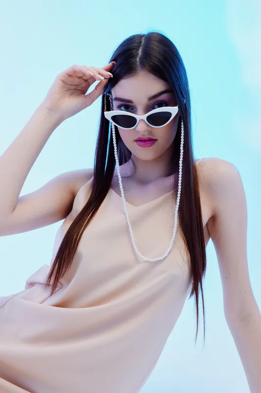 Woman beauty fashion model wearing white sunglasses and beige dress poses against blue background. Concept for style, elegance, and modern fashion photography.