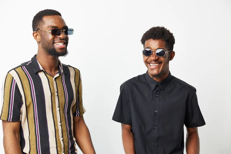 Portrait of black men smiling with sunglasses, wearing stylish shirts, conveying a sense of joy and friendship in a bright environment.