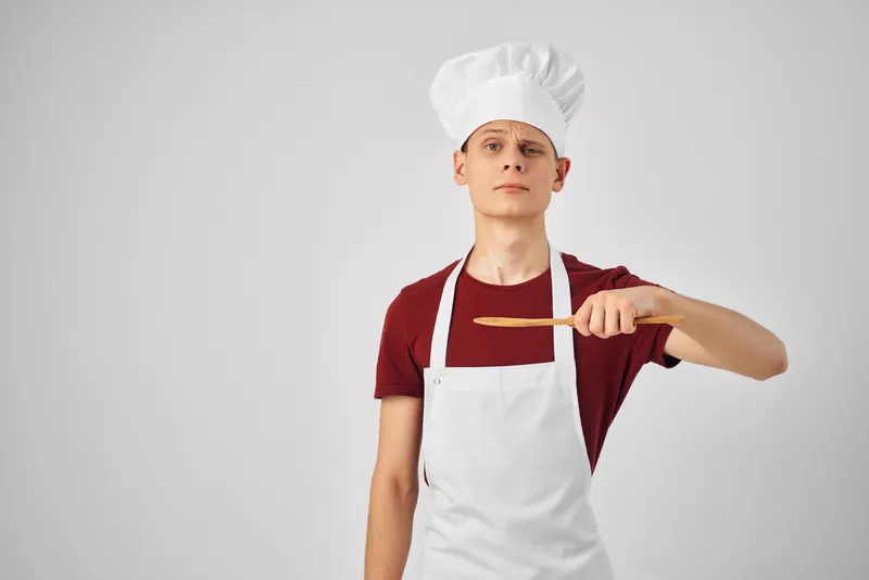 Мужчина в белом фартуке работает с кухонной утварью, занимаясь приготовлением пищи