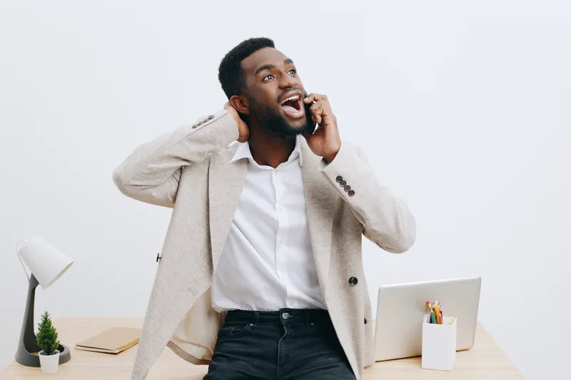 Smiling man talking on mobile phone in modern office, casual business attire, cheerful expression, work environment, young adult, professional, indoor, lifestyle concept