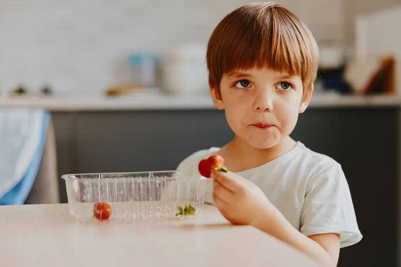Young boy enjoying fresh strawberries in a cozy kitchen setting, expressing curiosity and delight. Perfect for food-related themes and child-centric content.
