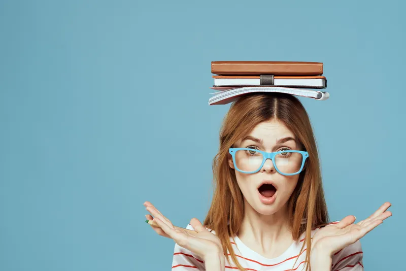 Студентка держит книги на голове на фоне синего цвета, что символизирует научное образование