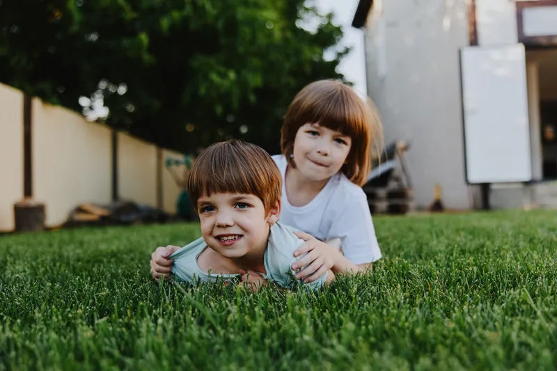 Two cheerful children playing on green grass, enjoying a sunny day outdoors, showcasing brotherly love and joy in a vibrant atmosphere.