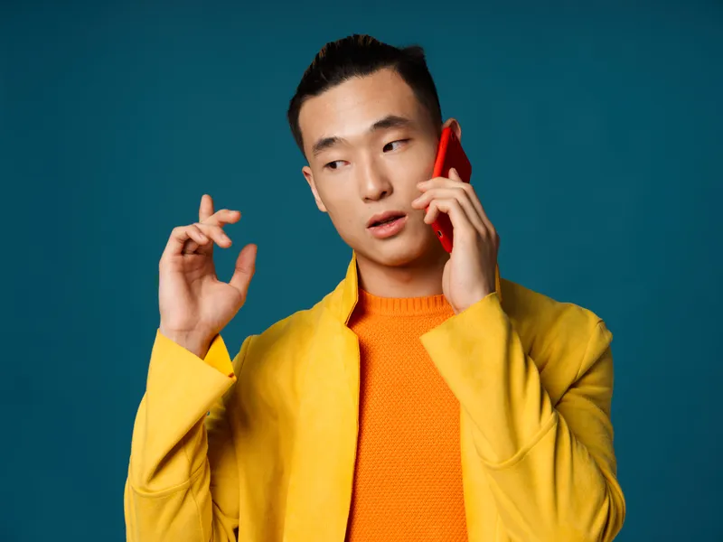 Мужчина в куртке на синем фоне жестикулирует руками и разговаривает по телефону