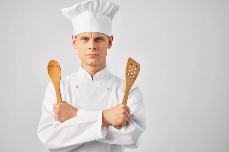 Мужчина в форме шеф-повара с кухонной утварью, на его лице читаются эмоции