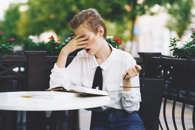 Женщина в очках читает книгу за столиком в ресторане, на заднем плане цветы