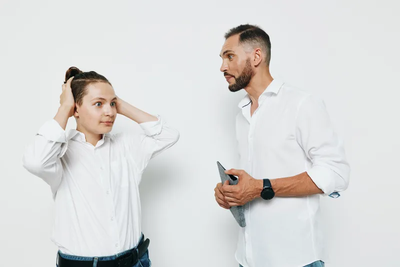 Professional man stands against an isolated colored background, exuding confidence and focus. A colleague adjusts his look, creating a moment of teamwork and leadership in a clean, modern corporate