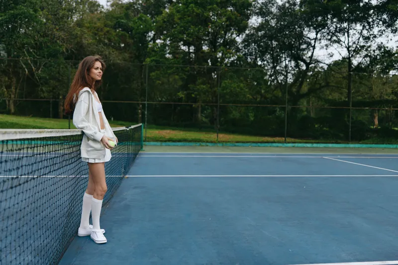 Young female tennis player in casual sportswear poses on court, showcasing confidence and athleticism, surrounded by a vibrant green background
