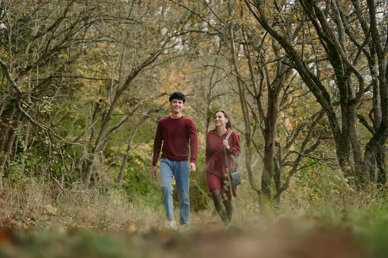 A young couple walking along a leafy forest trail in autumn, a candid scene highlighting authentic connection and genuine emotions, capturing natural everyday lifestyle and believable interaction.