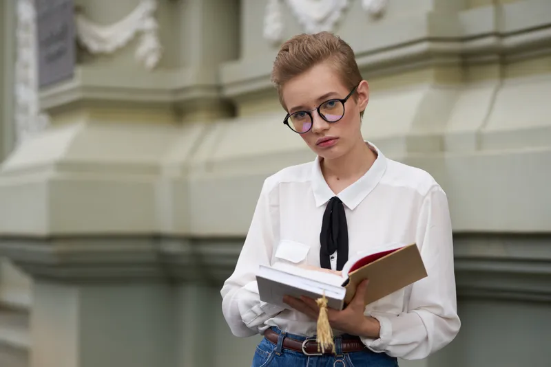 Студент с книгой в руках на открытом воздухе, читает