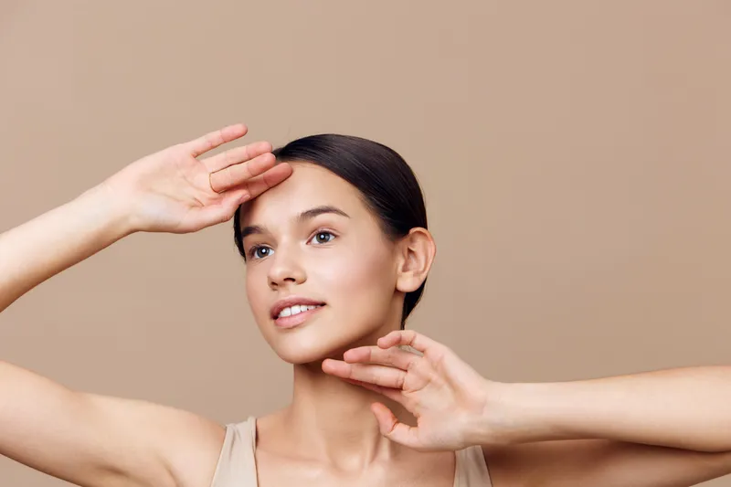 Fresh and natural portrait of a young woman with light brown skin, showcasing a joyful expression against a soft beige background, perfect for health and beauty themes