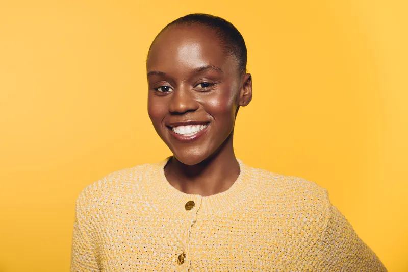 Smiling African woman with dark skin wearing a yellow sweater stands against a yellow background. Portrait of happiness, confidence, and natural beauty in studio lighting.
