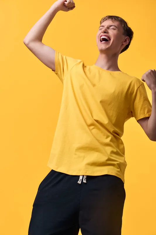 Joyful man in a yellow shirt celebrates with raised arms against a bright yellow backdrop, dynamic movement and exuberant energy conveying happiness, triumph and carefree lifestyle in a casual