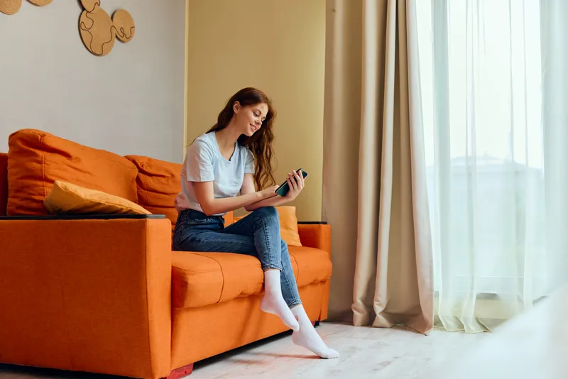Женщина болтает по смартфону, сидя на оранжевом диване
