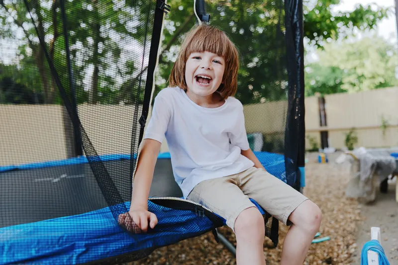 Happy boy enjoying time on a trampoline, surrounded by greenery and sunlight in a playful outdoor setting. Perfect for capturing childhood joy and fun activities.