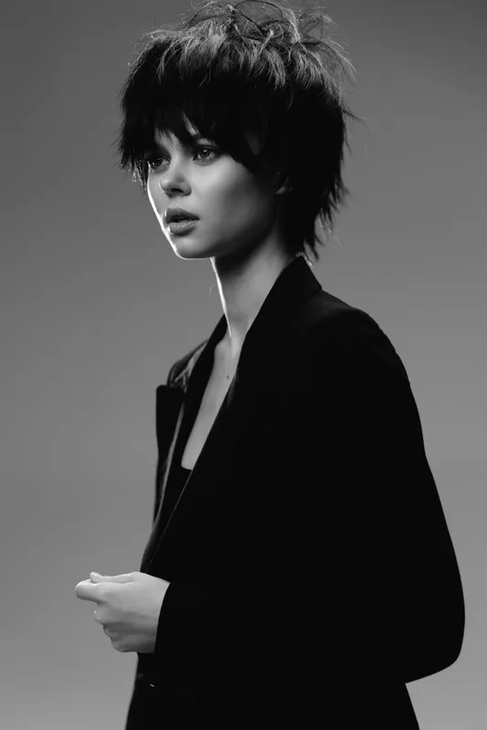 Black and white portrait of a young woman with short hair wearing a dark blazer, expressing thoughtful emotion in minimalist style.