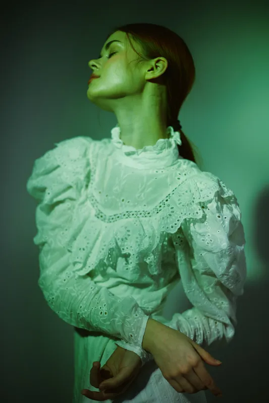 Ethereal portrait of a model in a vintage white lace blouse, embracing tranquility and elegance against a soft green backdrop, conveying a serene and peaceful emotion