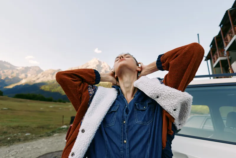 Woman jacket outdoors by car on road with mountain scenery, enjoying travel and relaxation, a scenic trip moment of freedom and adventure in nature landscape during holiday journey.