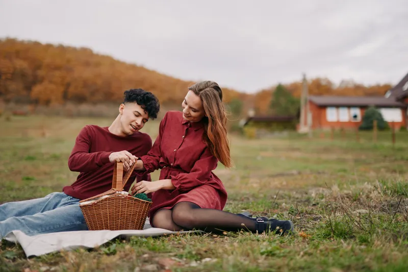 A candid, authentic moment of a young couple sharing a picnic on a blanket in a rustic field, portraying genuine connection, natural interaction and honest emotion for lifestyle storytelling.